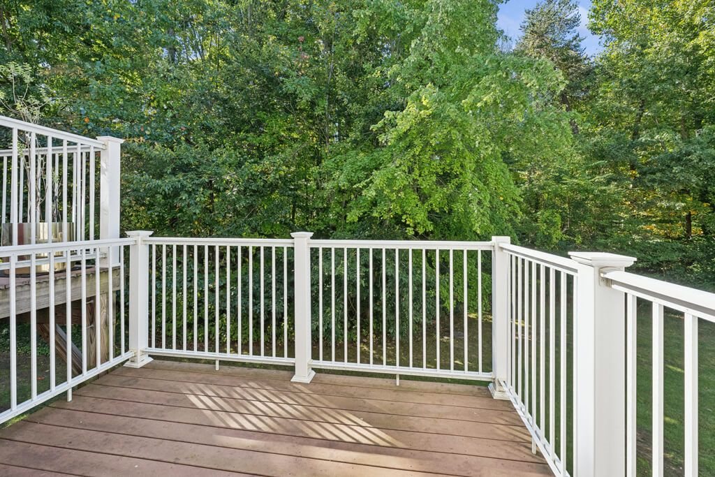 a deck with white railing and trees in the background